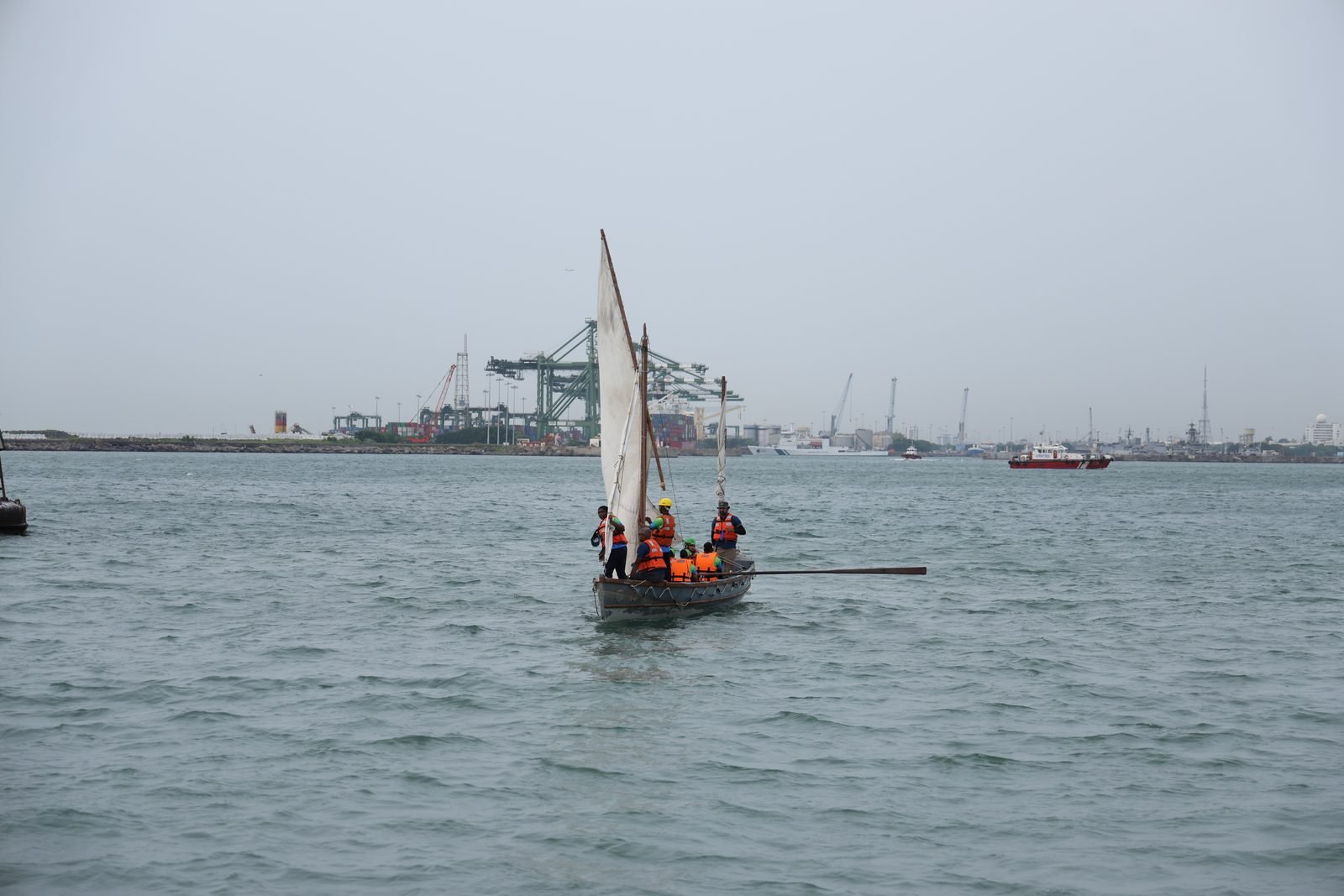 NCC whaler under full sail approaching Chennai port with container cranes on the horizon