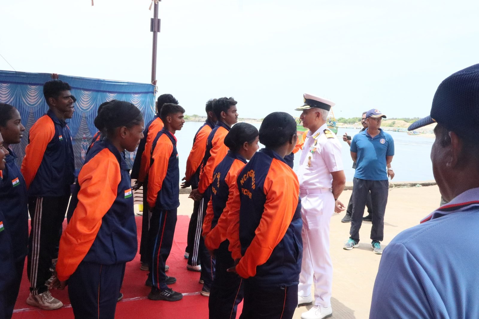 NCC cadets in orange-blue expedition jackets being briefed by a naval officer