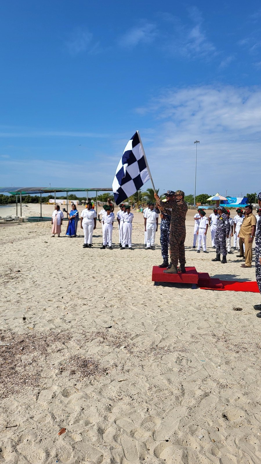 Officer on a red platform waving the checkered flag as the sailboat arrives at Thoothukudi